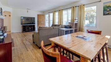 Ein Wohnzimmer mit einem Holzesstisch, einer Couch, einem Fernseher und einem Fenster mit Vorhängen.