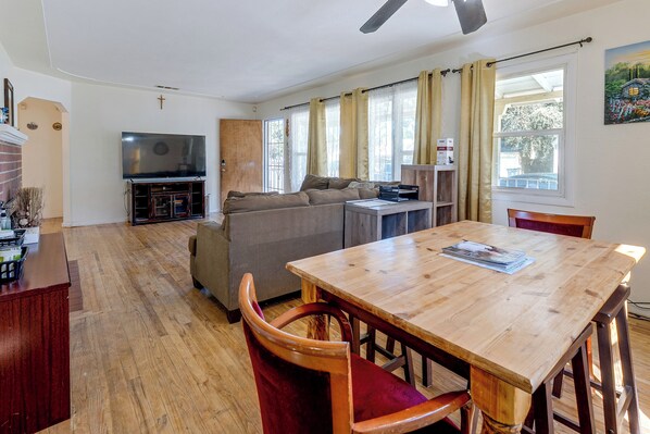 A living room with a wooden dining table, a sofa, a television, and a window with curtains.