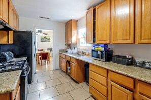 Cozinha com armários de madeira, fogão, micro-ondas e área de jantar com cadeiras e mesa.