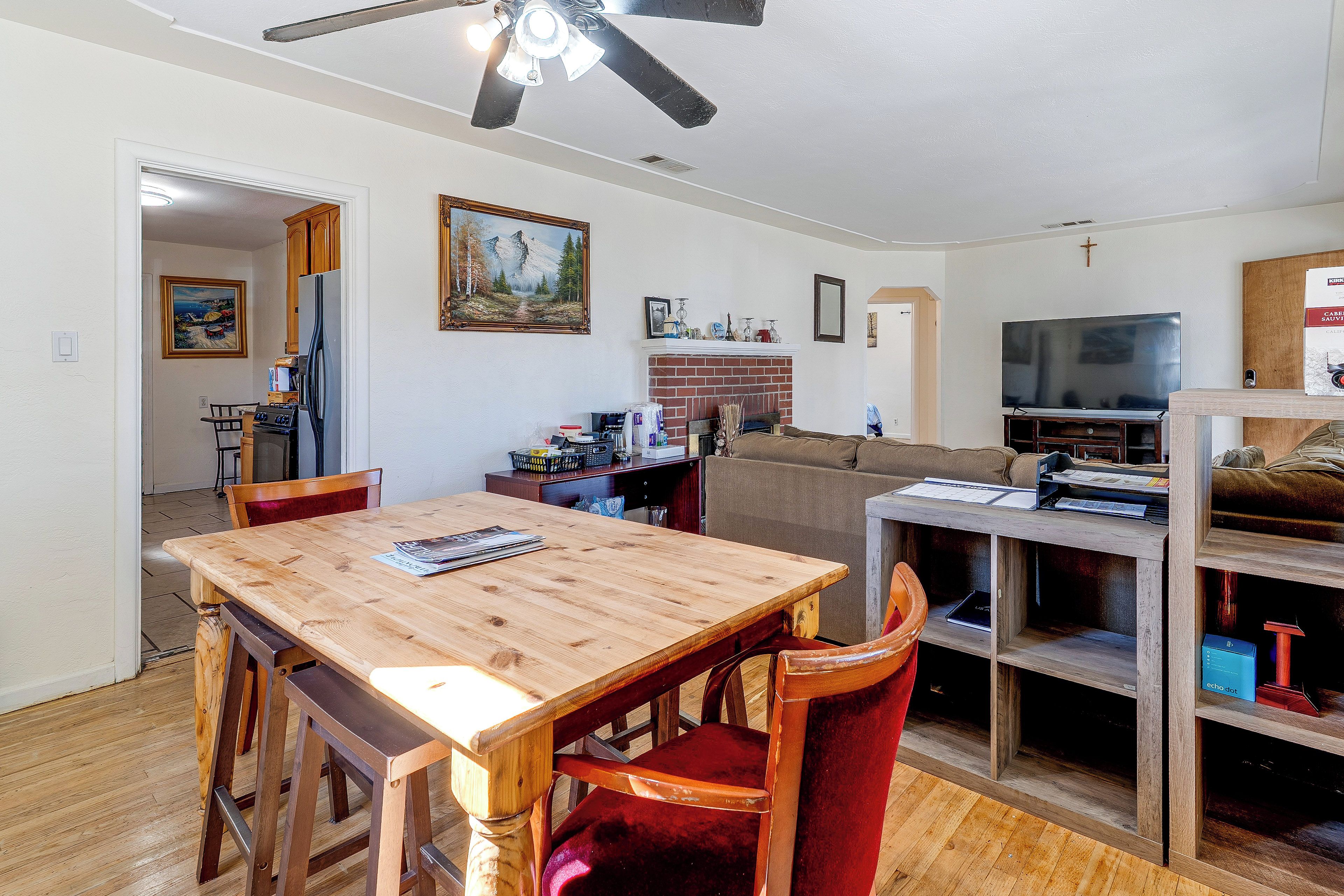 Un comedor con mesa y sillas de madera, una cocina al fondo, una chimenea y un televisor en la sala.