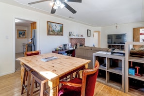 Ein Essbereich mit Holztisch und -stühlen, eine Küche im Hintergrund, ein Kamin und ein Fernseher im Wohnzimmer.