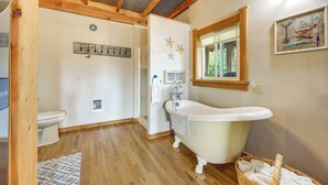 A bathroom with a clawfoot bathtub, a window, and a wooden ceiling.