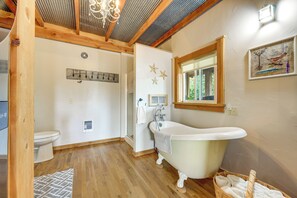 A bathroom with a clawfoot bathtub, a window, and a wooden ceiling.