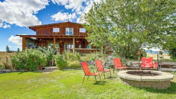 A wooden cabin with a porch, surrounded by a grassy yard and trees.