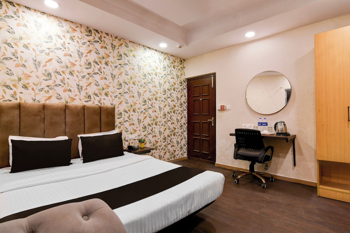 A hotel room with a large bed, a desk with a chair, a round mirror, and a wardrobe.