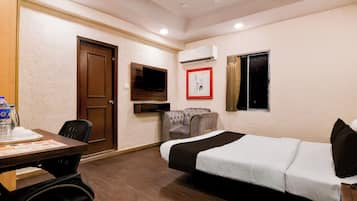 A hotel room with a bed, a desk with a chair, a television, an air conditioning unit, and a window with curtains.