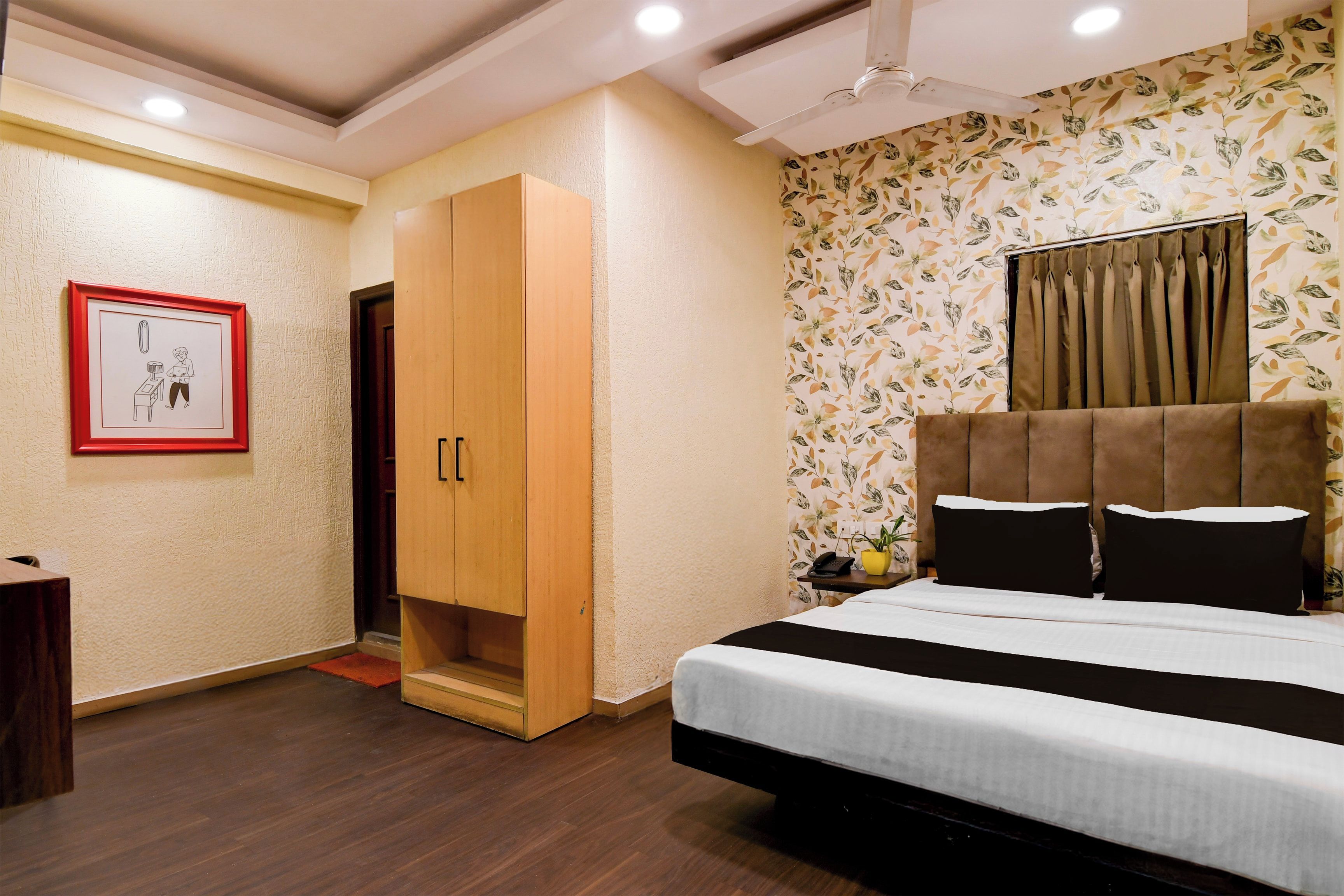 A bedroom with a bed, a wardrobe, a desk, a chair, a telephone, and a wall with a floral pattern.