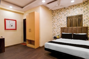 A bedroom with a bed, a wardrobe, a desk, a chair, a telephone, and a wall with a floral pattern. - Townhouse Parkstreet FormerlyHotel Royal (Kolkata)