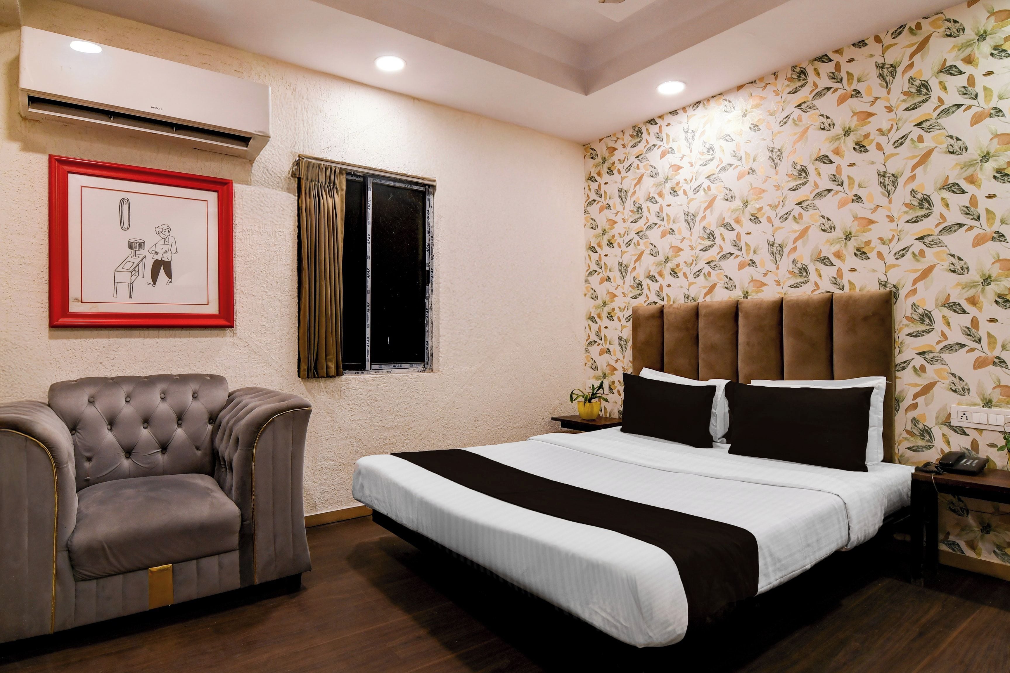 Habitación de hotel con cama, una silla, un cuadro enmarcado, una ventana y una pared con estampado floral.