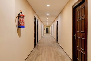 A hotel corridor with wooden flooring, doors on both sides, and a fire extinguisher mounted on the wall. - Townhouse Parkstreet FormerlyHotel Royal (Kolkata)
