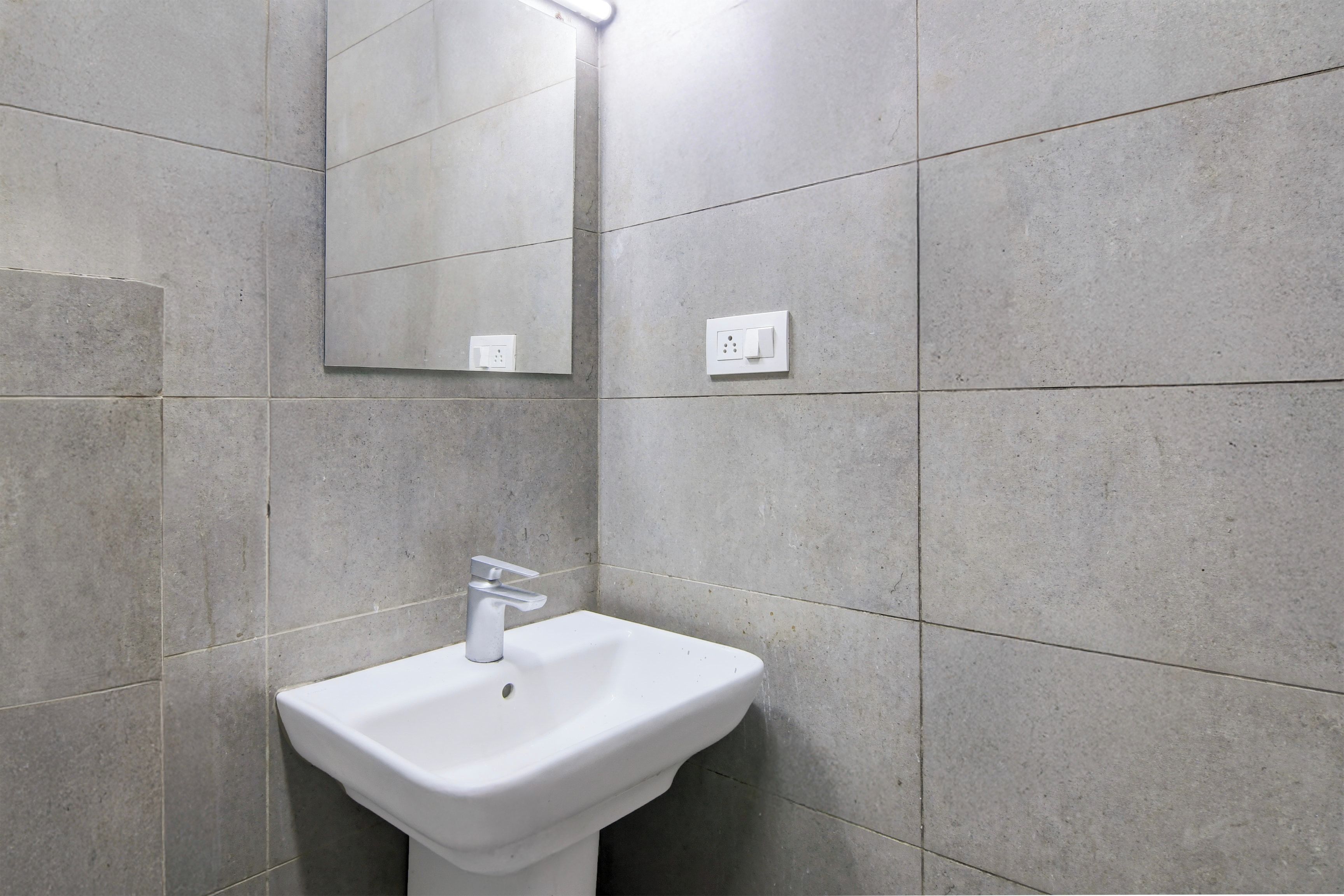 A bathroom with a white pedestal sink, a mirror, and a light fixture on the wall.