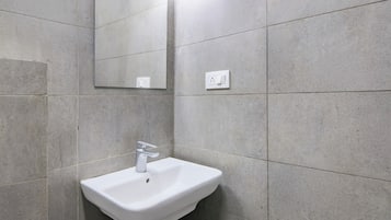 A bathroom with a white pedestal sink, a mirror, and a light fixture on the wall.