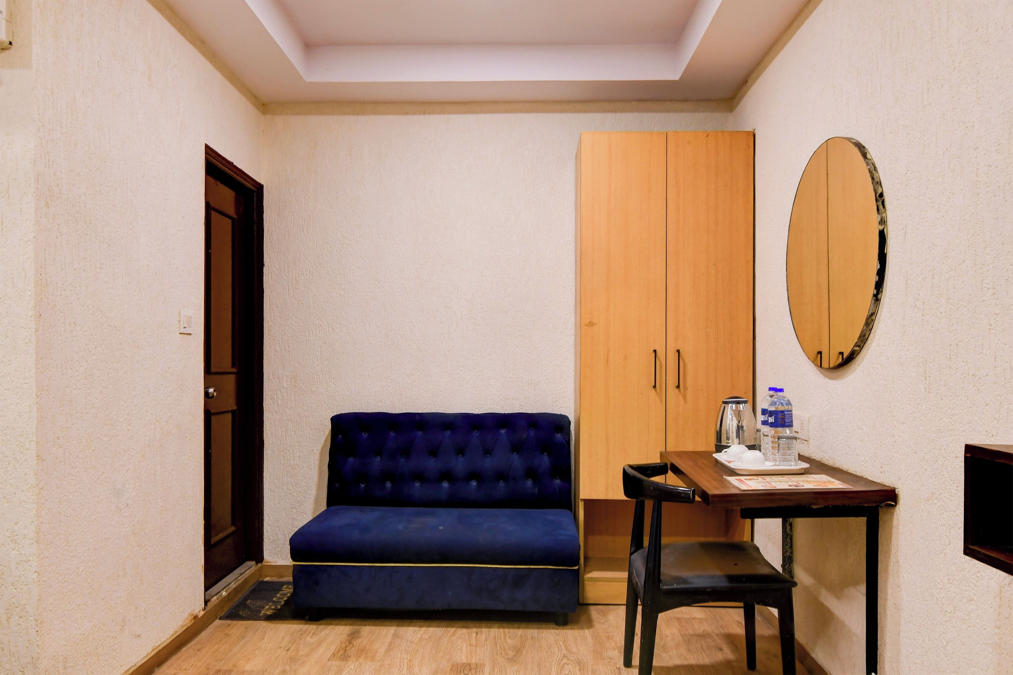 A room with a blue sofa, a wooden wardrobe, a small table with a kettle and cups, and a mirror on the wall.