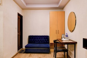 A room with a blue sofa, a wooden wardrobe, a small table with a kettle and cups, and a mirror on the wall. - Townhouse Parkstreet FormerlyHotel Royal (Kolkata)