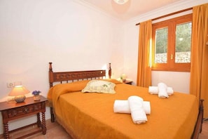 A neatly made bed with a headboard, a bedside table with a lamp, and a window with curtains. - Cabin in Muro with swimming pool (Muro)