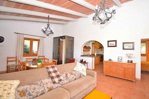 A living room with a sofa, dining table, and kitchen area visible through an archway. - Cabin in Muro with swimming pool (Muro)