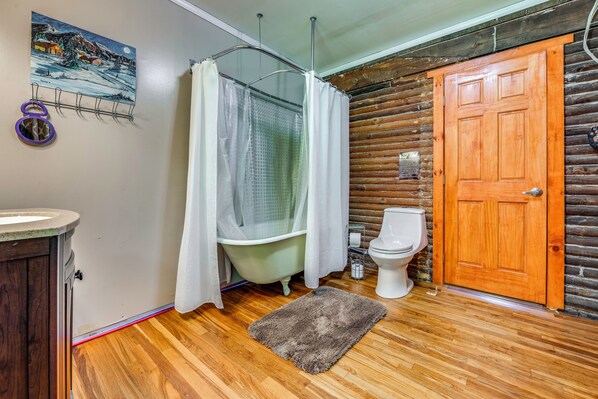 A bathroom with a wooden floor, a bathtub, a toilet, and a wooden door.