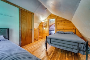 Ein Schlafzimmer mit geneigter Decke, Holzwänden, einem Bett mit Metallgestell und einer Tür zu einem anderen Raum.