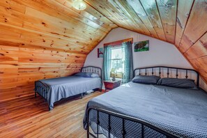 A cozy attic bedroom with wooden walls and sloped ceilings, featuring two beds with metal frames and patterned bedding. - 100-Acre Milan Cabin w/ Fire Pit & Shared Pond! (Milan)
