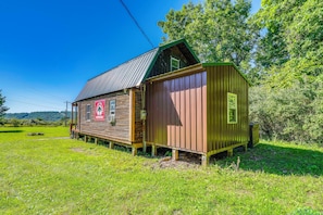 Eine rustikale Holzhütte mit einem Metalldach, gelegen auf einer grünen Wiese mit Bäumen im Hintergrund.