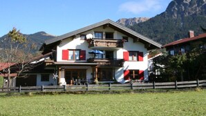 Un bâtiment à deux étages doté d’un balcon, d’une clôture en bois à l’avant et des montagnes en arrière-plan.