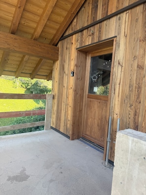 A wooden exterior wall with a door and window, a concrete floor, and a view of a green landscape. - Le Flocon de Neige votre parenthèse à la montagne (Les Avanchers-Valmorel)