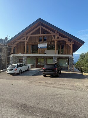 A two-story wooden building with a sign reading 'Atelier Alpin.' There are two cars parked in front. - Le Flocon de Neige votre parenthèse à la montagne (Les Avanchers-Valmorel)