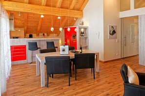 Eine moderne Küche mit Holzbalken, einem Essbereich mit Tisch und Stühlen und einer roten Akzentwand.