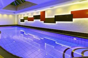 Ein Schwimmbecken mit Fliesenboden und einer Wand mit geometrischen Leuchten.