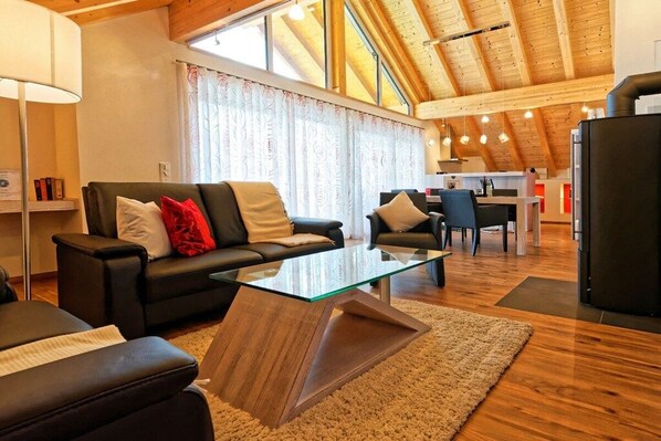 Ein modernes Wohnzimmer mit einem Glastisch, Ledersofas und einer Holzbalkendecke.