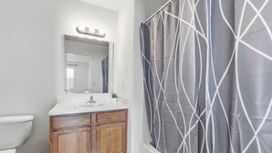 Un bagno con lavandino bianco, mobile contenitore in legno e tenda da doccia a motivo geometrico.