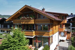 A multi-story wooden house with balconies, large windows, and a garden area. - Alpenflair holiday apartment 310 (Oberstdorf)
