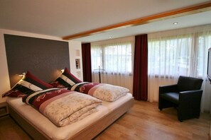 A bedroom with a bed, a chair, and a large window with curtains. - Alpenflair holiday apartment 310 (Oberstdorf)