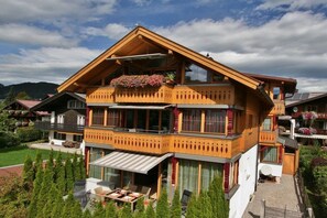 A two-story wooden chalet with a balcony, large windows, and a garden area. - Alpenflair holiday apartment 310 (Oberstdorf)