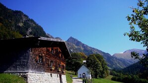 Ein traditionelles Chalet mit Steinunterbau, Holzbauweise und einem kleinen, angrenzenden weißen Gebäude, vor einer Berglandschaft.