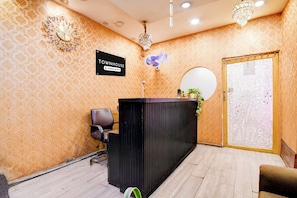 Un área de recepción con un mostrador negro, un cartel que dice 'TOWNHOUSE Company Serviced', un ventilador, un espejo y una puerta con un diseño de mosaico.