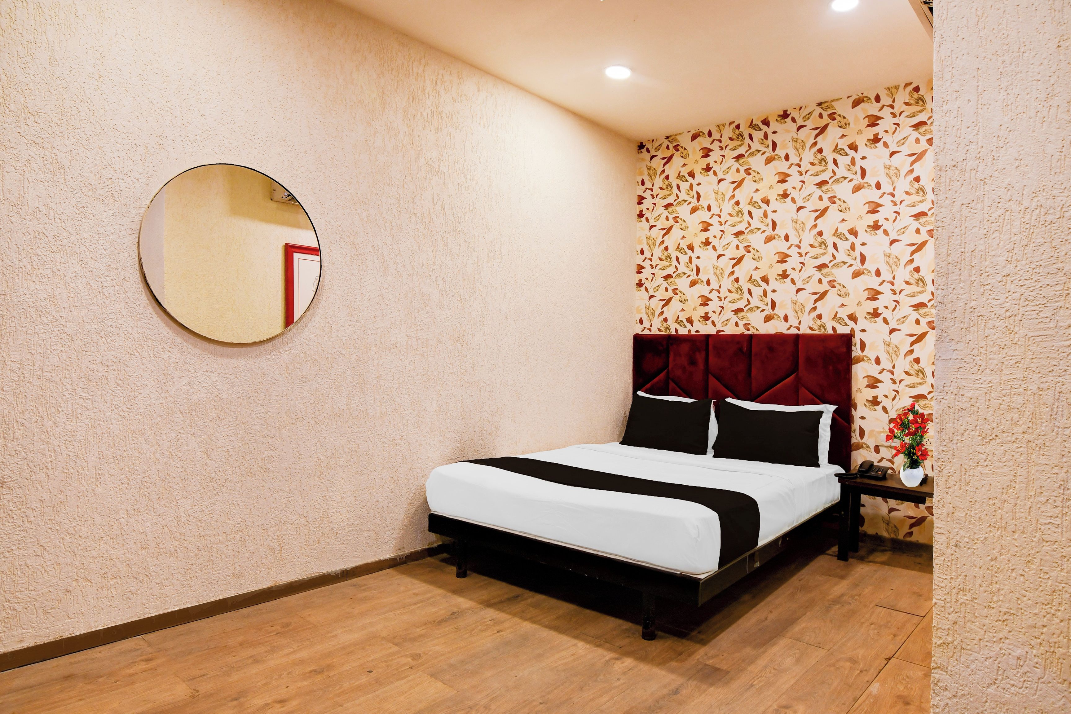 Quarto de hotel com uma cama, um espelho redondo, uma mesa de cabeceira com um telefone e papel de parede floral.