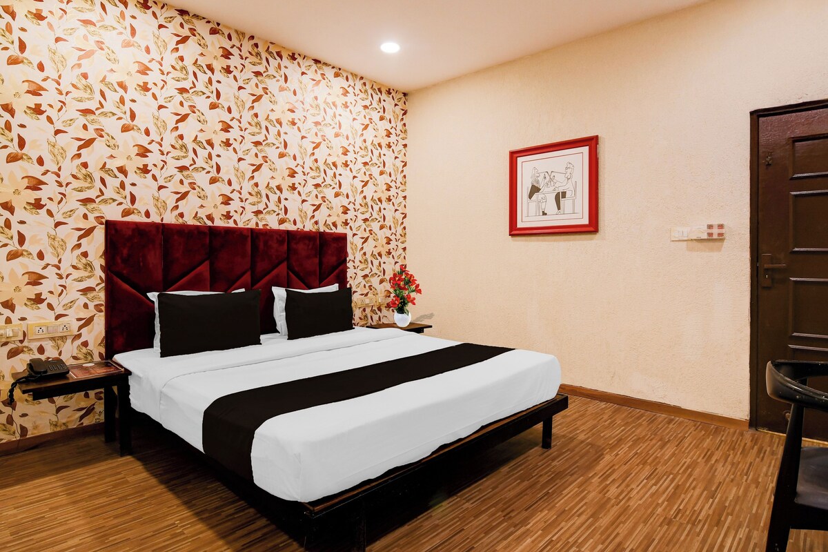 Una habitación de hotel con una cama, una mesita de noche, un teléfono, un cuadro en la pared y una puerta.