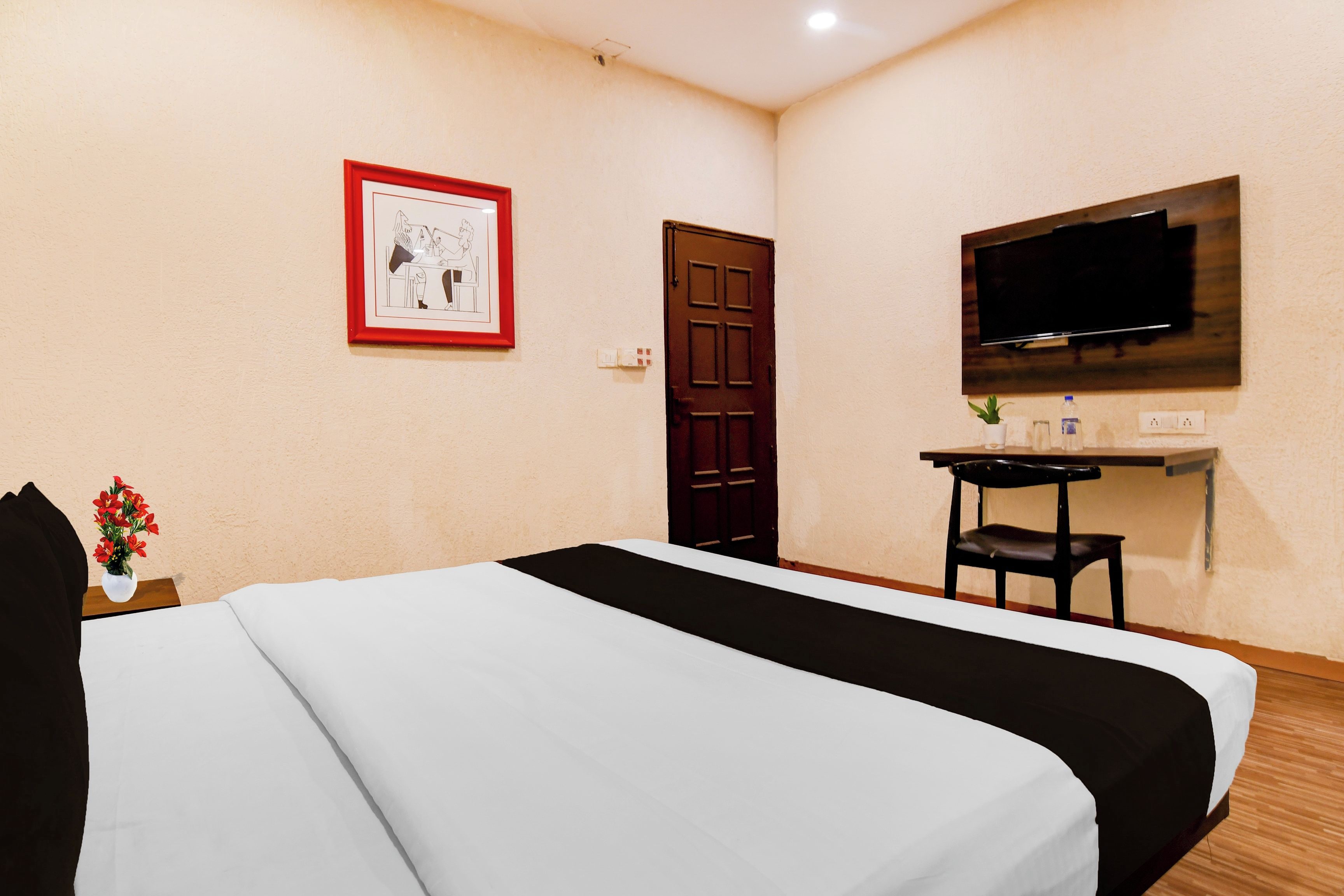 A hotel room with a bed, a desk, a television, and a door.
