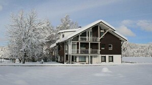 Um edifício de dois andares com varanda, rodeado por árvores cobertas de neve.