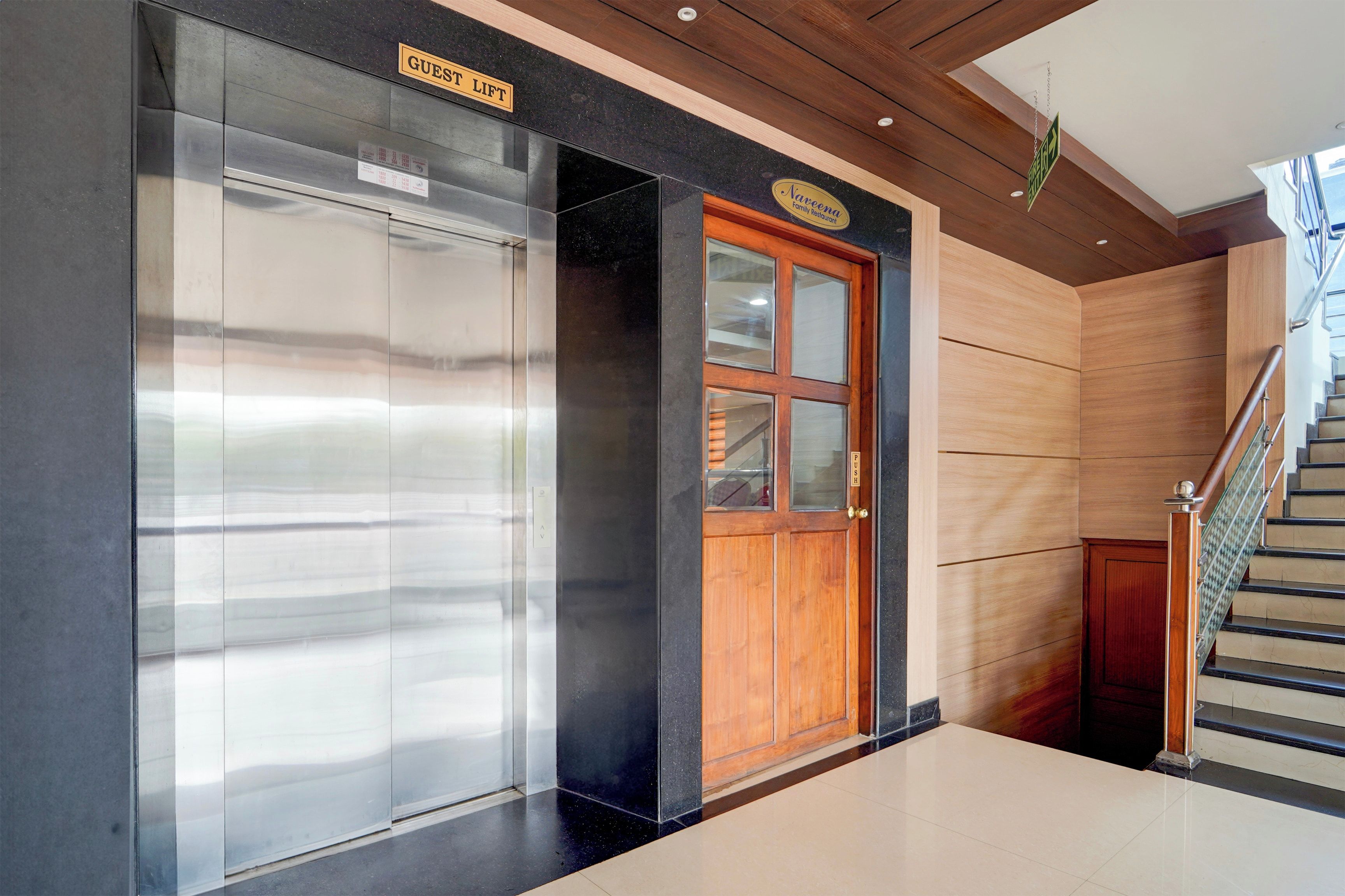 A hotel lobby with a guest lift, a wooden door, and a staircase.