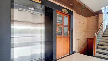 A hotel lobby with a guest lift, a wooden door, and a staircase.