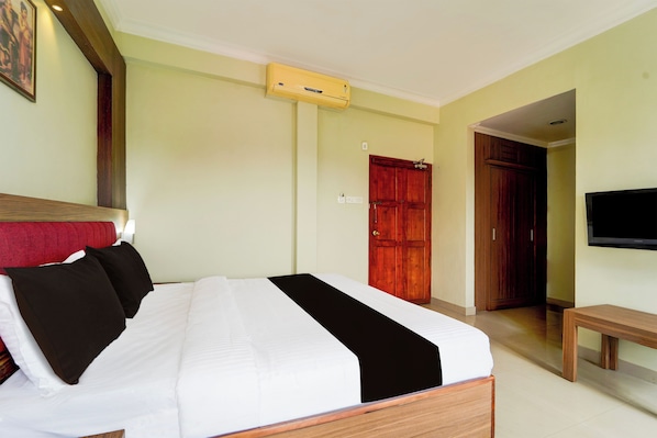 A hotel room with a bed, a bench, a television, and a door.