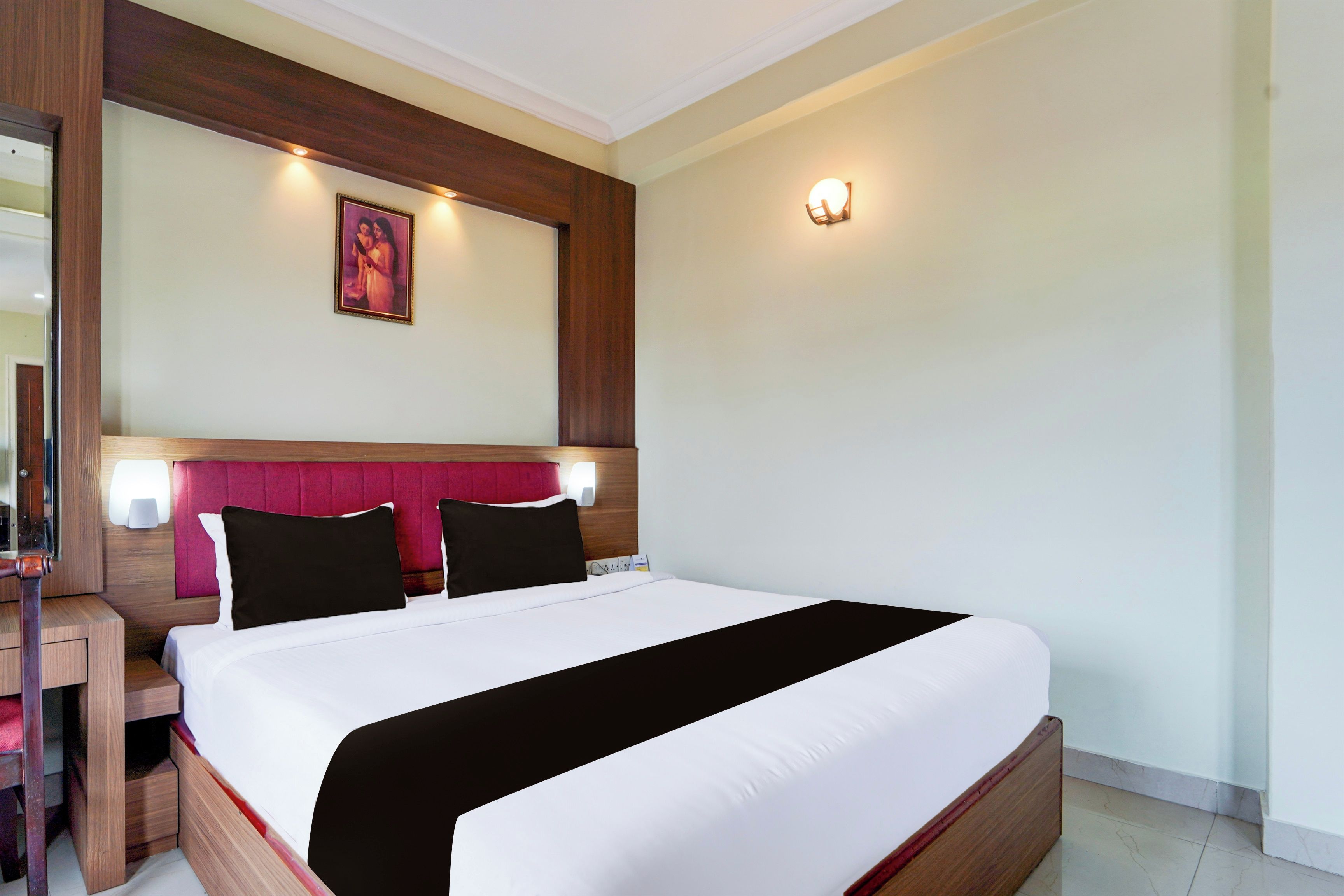 Habitación de hotel con una cama grande, cabecera de madera, mesita de noche y lámpara de pared.