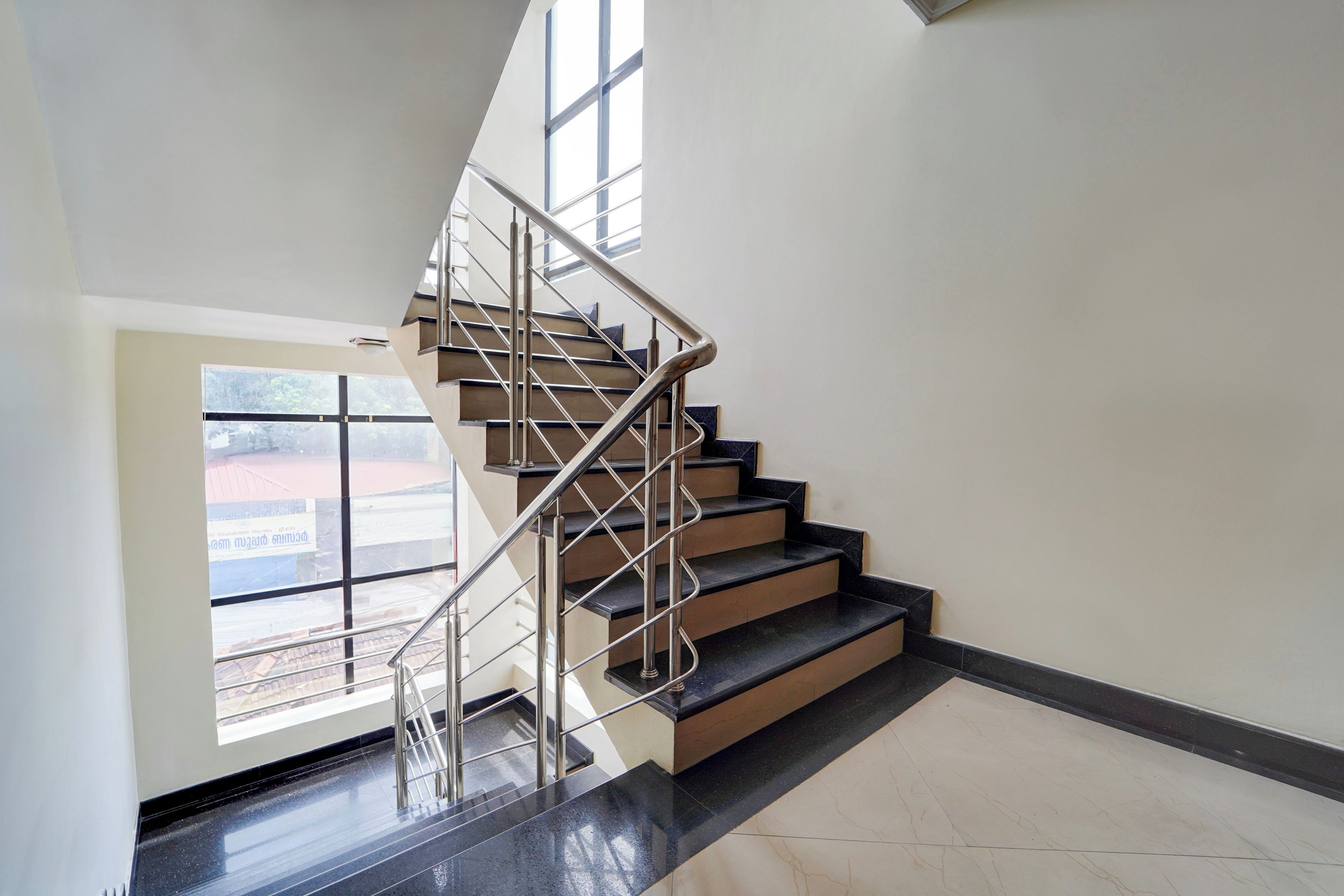 Una escalera moderna con barandillas metálicas y un portón de vidrio que da a un área exterior.