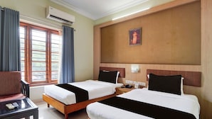 Habitación de hotel con dos camas, un escritorio, una silla y una ventana con cortinas.