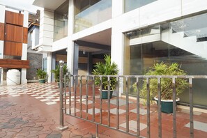 A modern building with a checkered floor, potted plants, and a metal fence.
