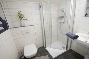 Ein modernes Badezimmer mit einer gläsernen Duschkabine, einer weißen Toilette, einem Waschbecken und einer kleinen Pflanze an der Wand.
