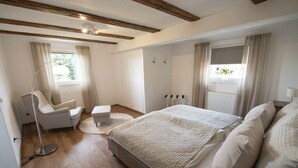 A bedroom with a bed, a chair, a floor lamp, and a window with curtains. - Holiday apartment with 1 bedroom (Oberkirch, Deutschland)
