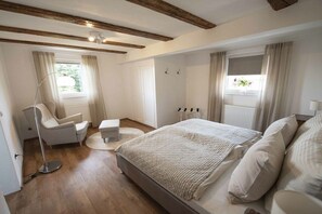 Ein Schlafzimmer mit Bett, Stuhl, Stehlampe und einem Fenster mit Vorhängen.